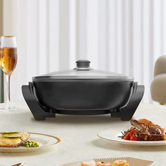 Black electric skillet on a table with plates of food and a glass of wine.